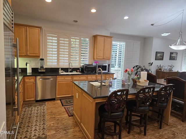 kitchen featuring pendant lighting, a kitchen island with sink, sink, appliances with stainless steel finishes, and light hardwood / wood-style floors