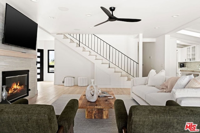 living room with ceiling fan, light wood-type flooring, and a tile fireplace