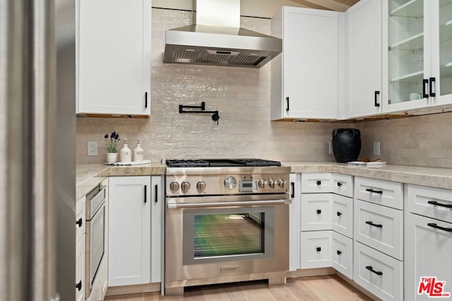 kitchen with tasteful backsplash, white cabinetry, stainless steel stove, and wall chimney range hood