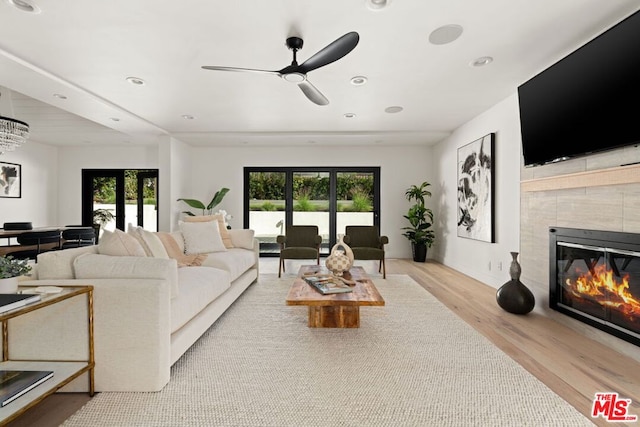 living room featuring ceiling fan with notable chandelier, light hardwood / wood-style flooring, a wealth of natural light, and a tiled fireplace