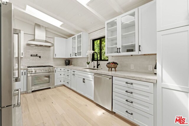 kitchen with white cabinets, sink, stainless steel appliances, and wall chimney range hood