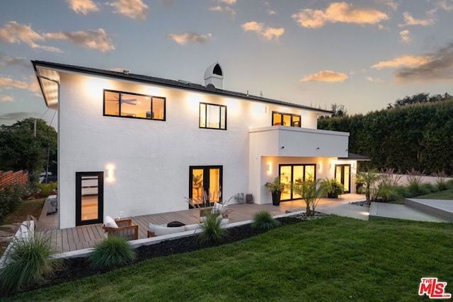 back house at dusk with a patio area, a balcony, and a yard