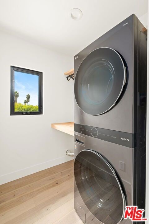 laundry area with light wood-type flooring and stacked washing maching and dryer