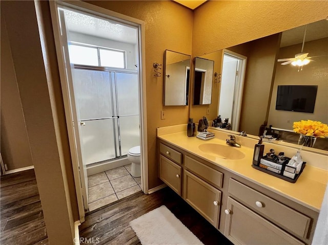 bathroom with ceiling fan, hardwood / wood-style floors, toilet, vanity, and a shower with shower door