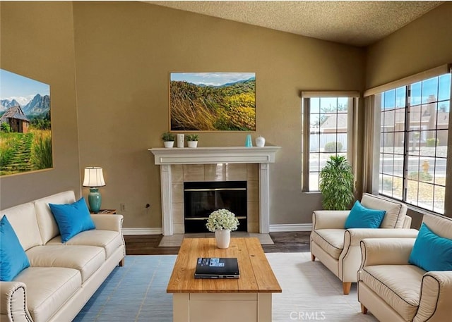 living room with hardwood / wood-style flooring, lofted ceiling, a textured ceiling, and a tiled fireplace