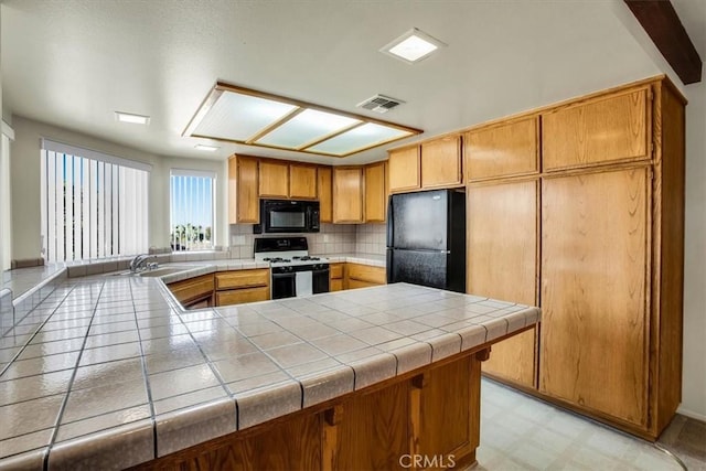 kitchen featuring sink, kitchen peninsula, tile countertops, decorative backsplash, and black appliances