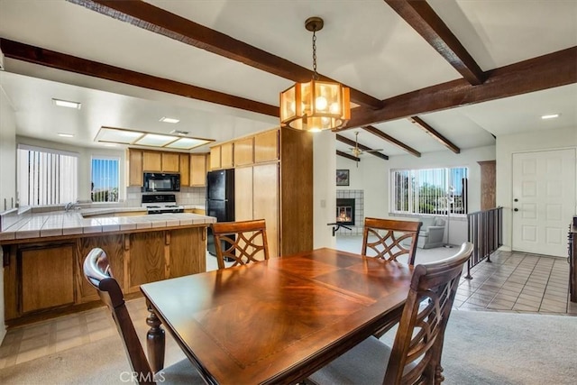 dining area featuring lofted ceiling with beams, light tile patterned floors, ceiling fan with notable chandelier, and a tiled fireplace