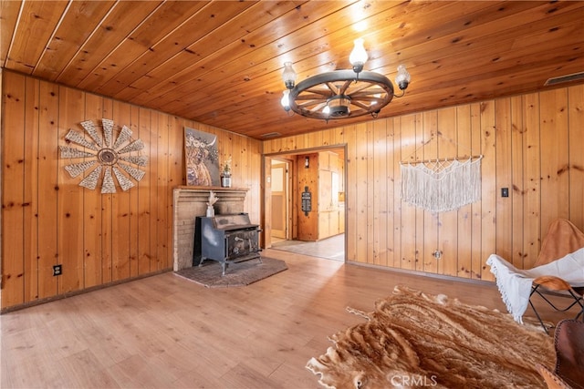 unfurnished living room with wood walls, light hardwood / wood-style floors, a wood stove, and wooden ceiling