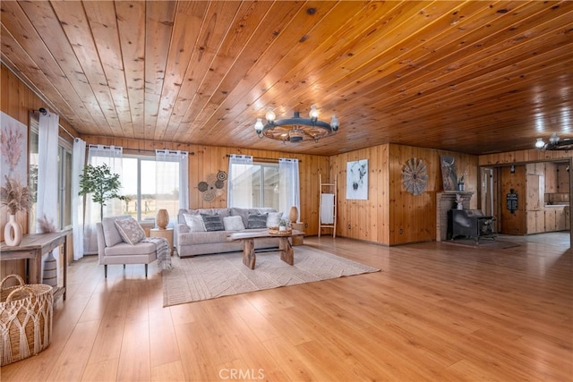 living room featuring a wood stove, an inviting chandelier, wooden walls, wood ceiling, and light wood-type flooring