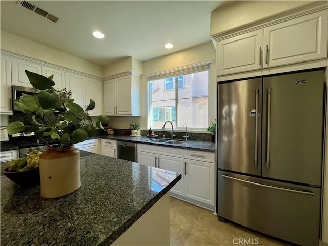 kitchen featuring light tile patterned floors, white cabinetry, stainless steel appliances, dark stone counters, and sink