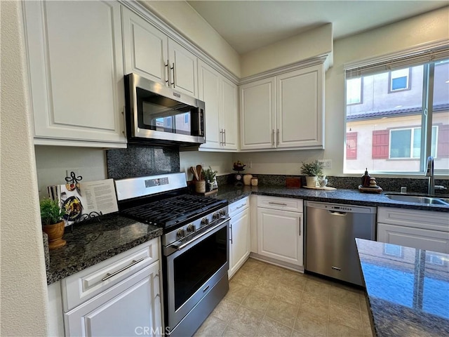 kitchen featuring appliances with stainless steel finishes, dark stone countertops, white cabinetry, and sink