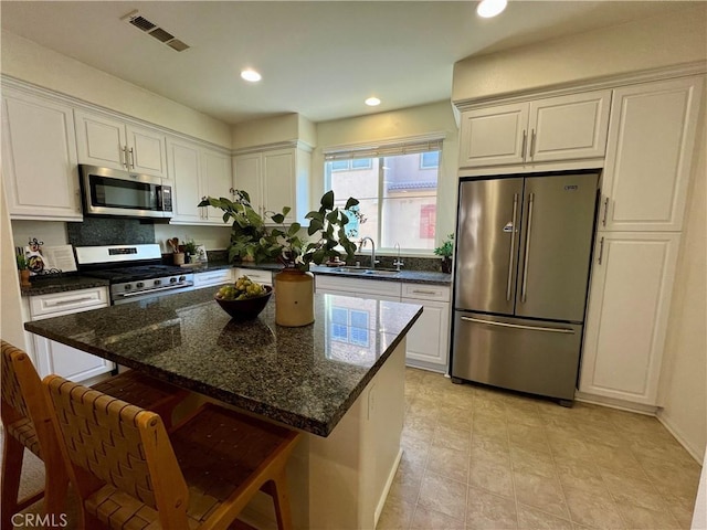 kitchen with stainless steel appliances, backsplash, sink, dark stone counters, and a center island