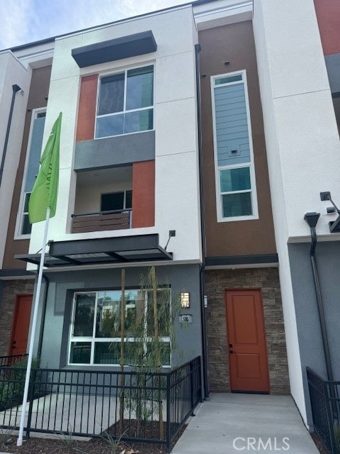 view of front facade with stone siding, fence, and stucco siding