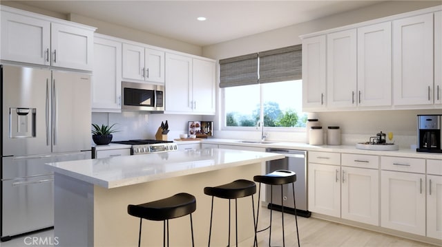 kitchen with a breakfast bar, a sink, white cabinetry, appliances with stainless steel finishes, and a center island