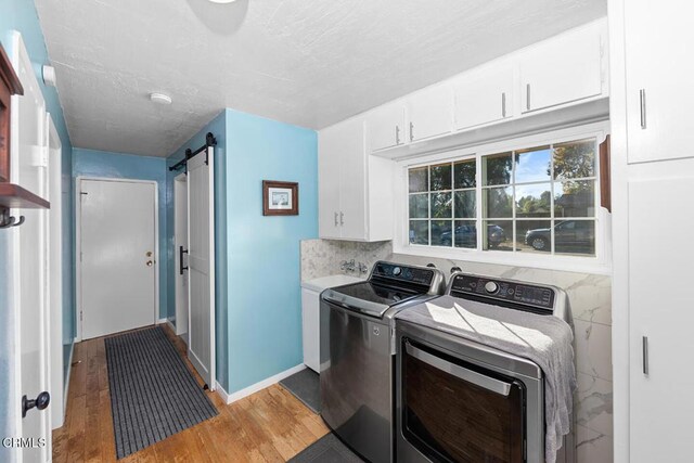 laundry area with cabinet space, a barn door, wood finished floors, independent washer and dryer, and a textured ceiling