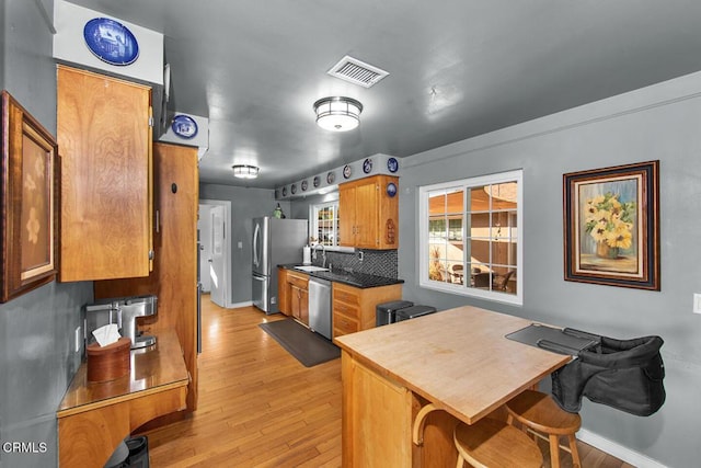 kitchen featuring visible vents, appliances with stainless steel finishes, brown cabinets, light wood-type flooring, and backsplash