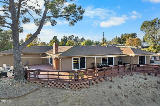 rear view of property with roof with shingles, a chimney, a wooden deck, and stucco siding