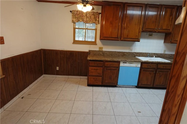 kitchen with ceiling fan, dishwasher, wood walls, sink, and light tile patterned floors