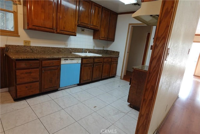 kitchen with light tile patterned floors, backsplash, dark stone countertops, dishwasher, and sink