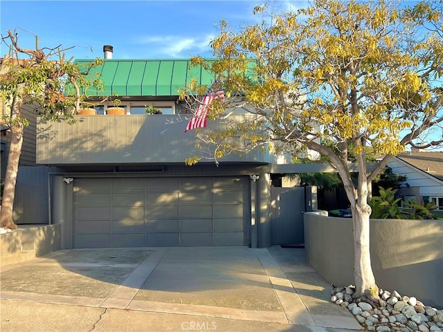 exterior space with fence, concrete driveway, metal roof, a garage, and a standing seam roof