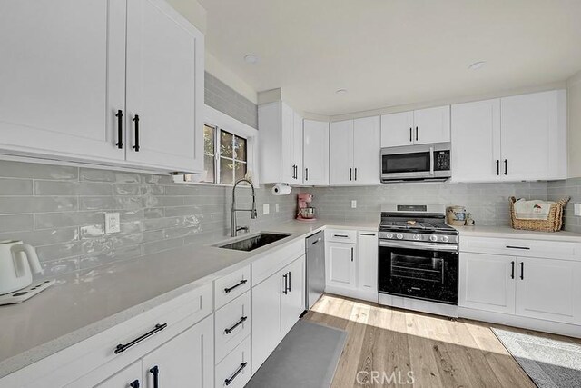 kitchen with sink, white cabinets, stainless steel appliances, and light hardwood / wood-style floors