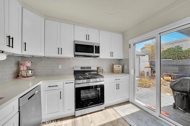 kitchen with white cabinets, light wood-type flooring, stainless steel appliances, and tasteful backsplash