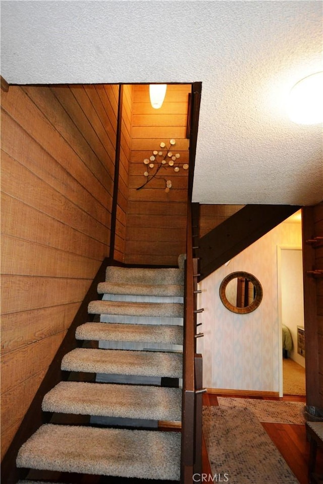 stairs with a textured ceiling and wooden walls