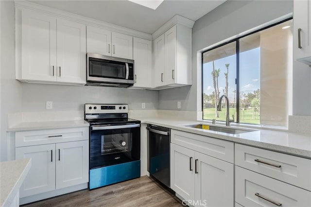 kitchen with sink, light hardwood / wood-style flooring, light stone countertops, white cabinetry, and stainless steel appliances