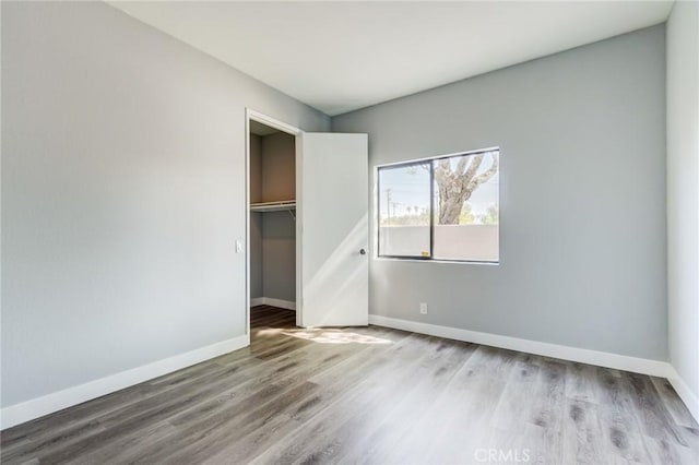 unfurnished bedroom with a walk in closet, a closet, and hardwood / wood-style floors