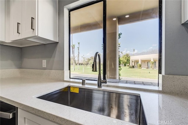 kitchen featuring a healthy amount of sunlight, light stone countertops, white cabinetry, and sink