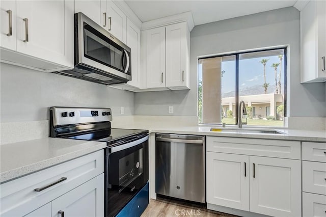 kitchen featuring sink, light stone countertops, appliances with stainless steel finishes, light hardwood / wood-style floors, and white cabinetry