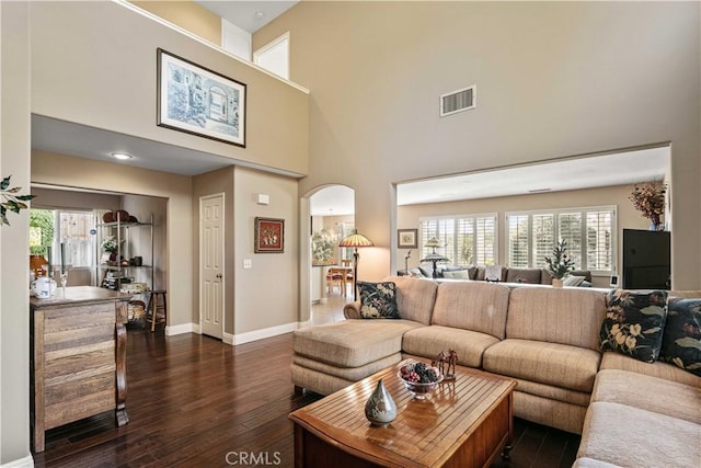 living room with dark wood-type flooring, a healthy amount of sunlight, and a towering ceiling