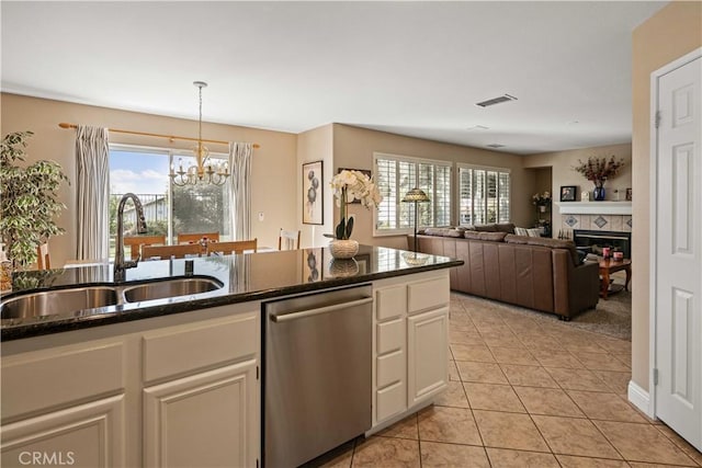 kitchen with a tiled fireplace, dark stone counters, stainless steel dishwasher, white cabinets, and sink