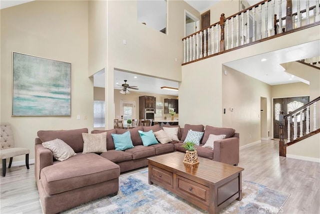 living room with ceiling fan, a towering ceiling, and light wood-type flooring