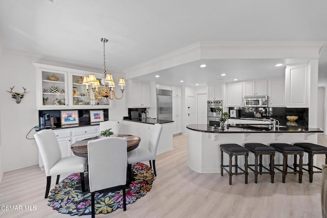 dining area featuring sink, light wood-type flooring, ornamental molding, and a chandelier