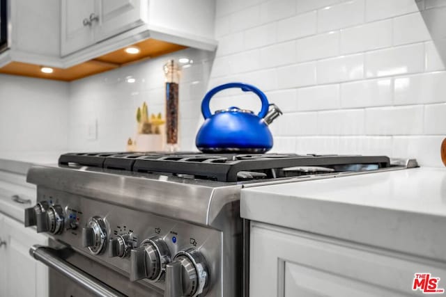 details with decorative backsplash, white cabinetry, and high end stainless steel range