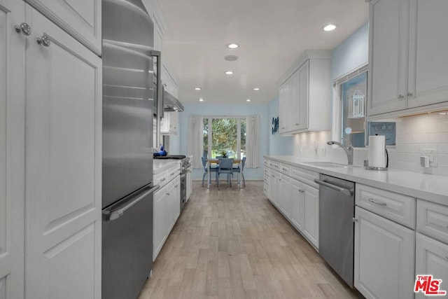 kitchen with high end appliances, sink, tasteful backsplash, light hardwood / wood-style floors, and white cabinetry