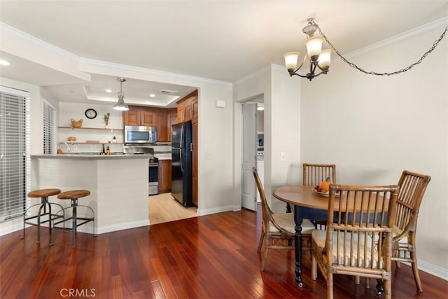 dining room featuring sink, a notable chandelier, crown molding, light hardwood / wood-style floors, and a tray ceiling