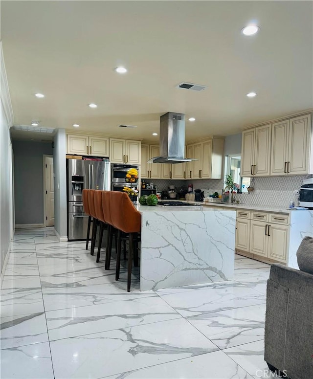 kitchen with cream cabinets, ventilation hood, appliances with stainless steel finishes, tasteful backsplash, and a kitchen bar