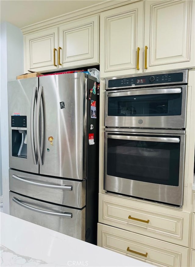 kitchen featuring cream cabinetry, light stone counters, and appliances with stainless steel finishes