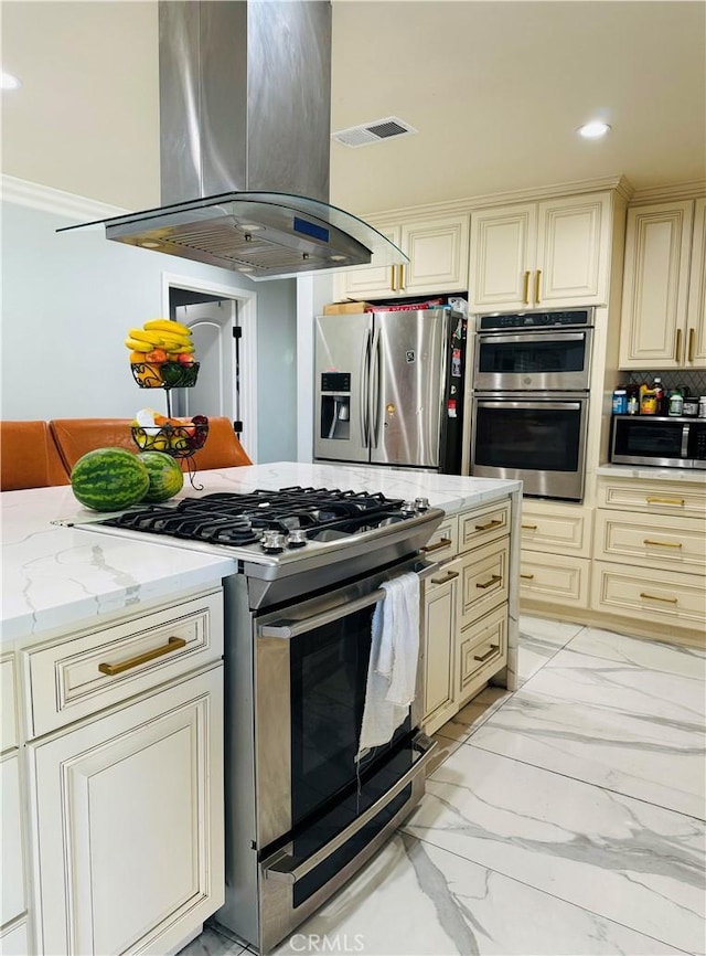 kitchen featuring light stone counters, island exhaust hood, appliances with stainless steel finishes, and cream cabinets