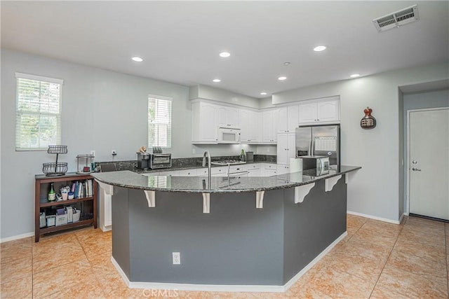 kitchen with dark stone countertops, stainless steel fridge, plenty of natural light, and white cabinets