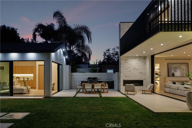 yard at dusk featuring an outdoor stone fireplace, area for grilling, a balcony, and a patio