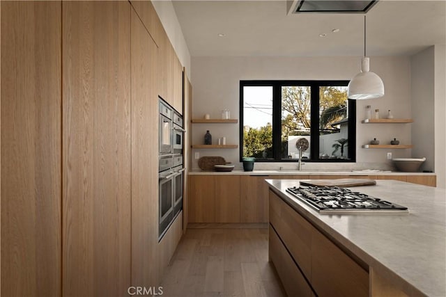 kitchen with light brown cabinetry, hanging light fixtures, light hardwood / wood-style floors, and stainless steel gas stovetop