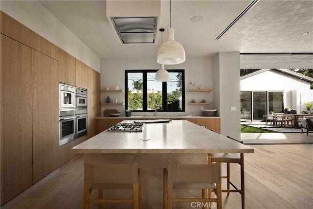 kitchen featuring appliances with stainless steel finishes, light wood-type flooring, a center island, hanging light fixtures, and a breakfast bar area