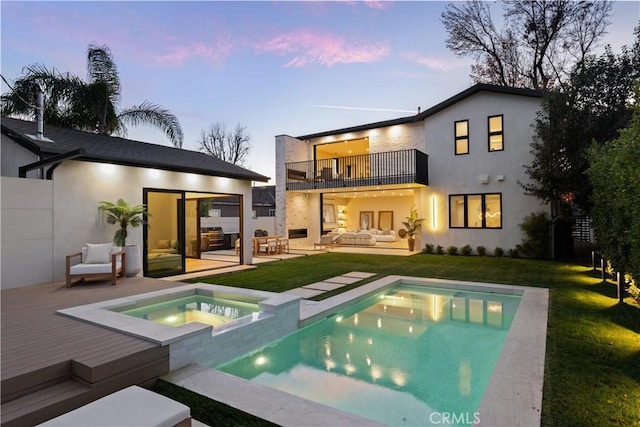 back house at dusk with an outdoor hangout area, a balcony, a swimming pool with hot tub, a patio area, and a lawn