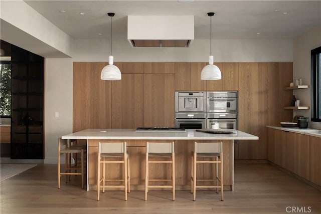 kitchen with decorative light fixtures, stainless steel appliances, a spacious island, and light hardwood / wood-style floors