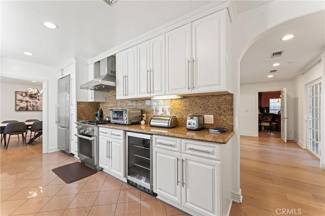 kitchen featuring white cabinets, wall chimney exhaust hood, beverage cooler, and appliances with stainless steel finishes