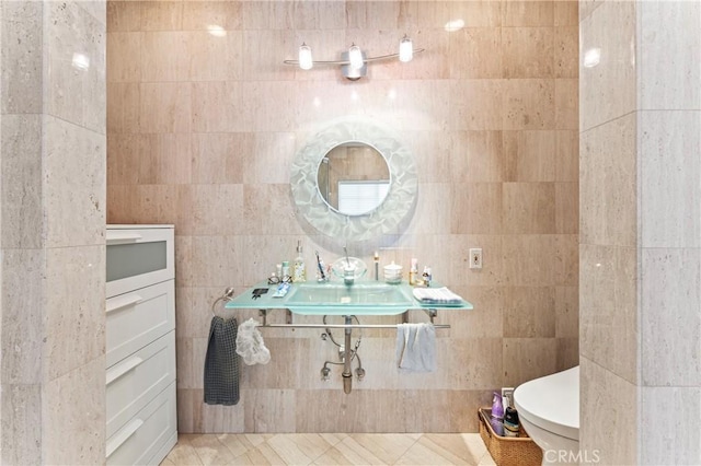 bathroom featuring toilet, tile patterned flooring, tile walls, and sink