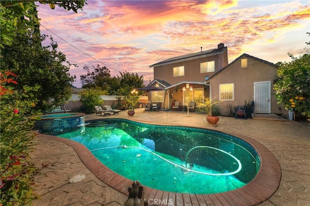 pool at dusk with a patio area and an in ground hot tub